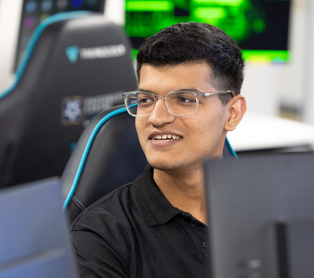 Hammad Jabeen working in a modern cybersecurity lab, seated at a desk with multiple computer monitors displaying code and digital interfaces.