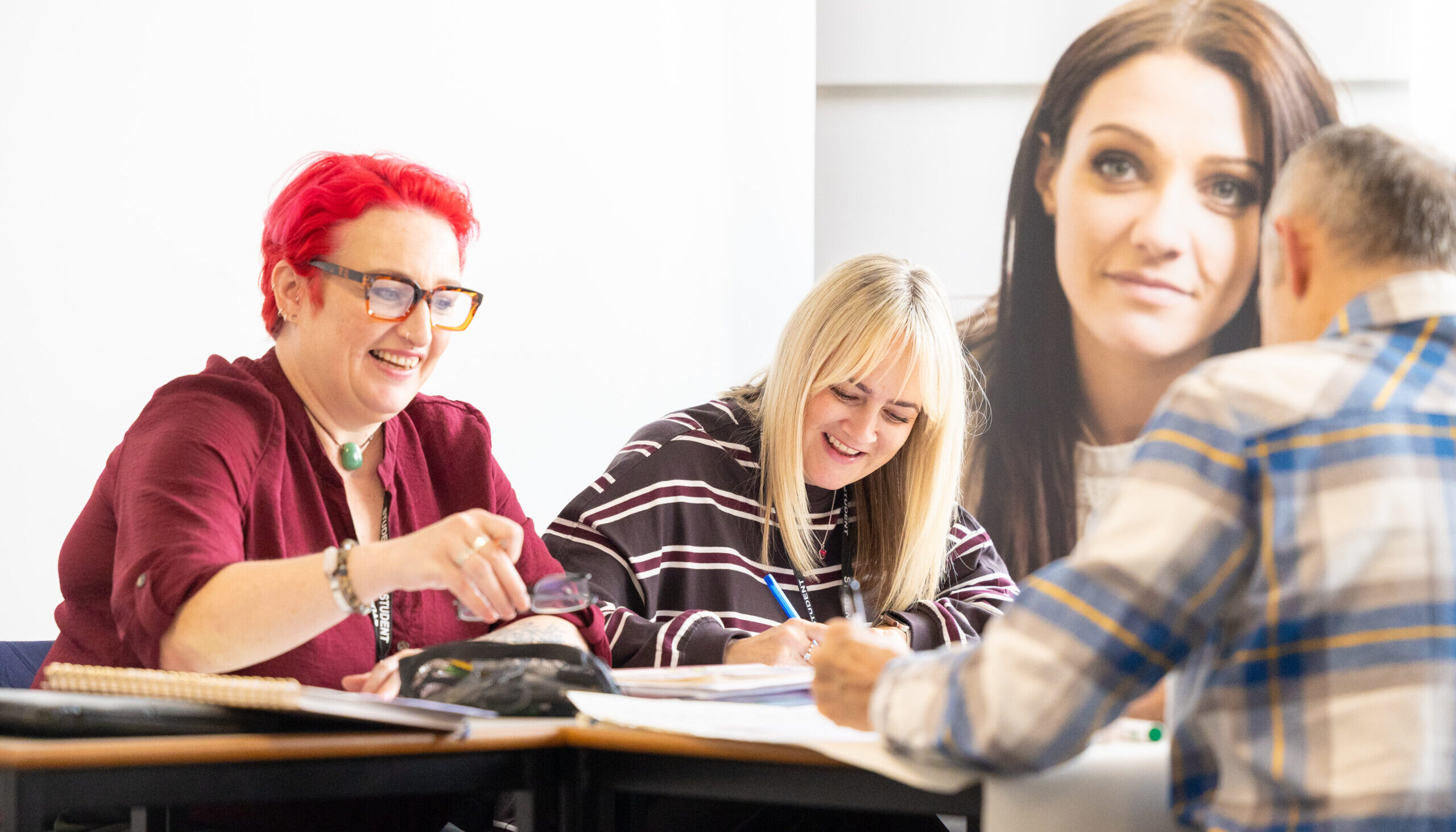 Person seated at a desk holding a pencil and writing on paper, with another person pointing at the documents during a discussion.
